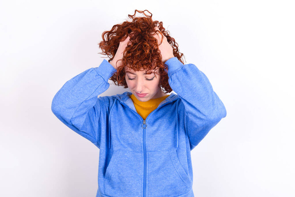 fiatal vörös hajú lány visel kék kabát felett fehér háttér tartó fej kezével, szenved a súlyos fejfájás, nyomja ujjak halántékok - Fotó, kép
