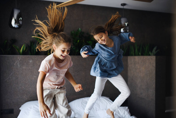Two little sister jumping on bed indoors in hotel. - Photo, image