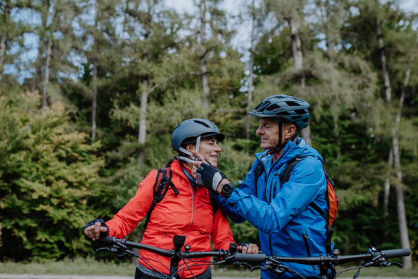 Senior couple bikers putting on cycling helmet outdoors in forest in autumn day. - Foto, immagini