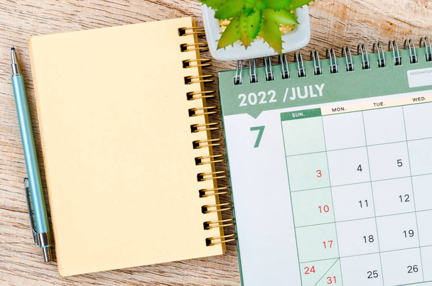 July 2022 desk calendar and diary with small plant on wooden background. - Foto, Bild