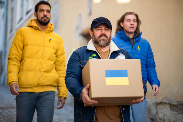 Team of volunteers collecting boxes with Humanitarian aid for Ukrainian immigrants in street - Fotó, kép