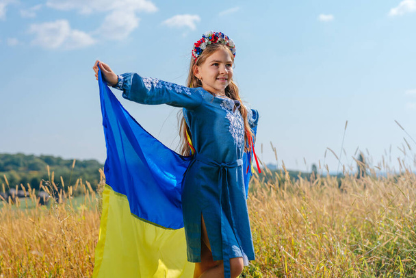 Girl wearing national dress and wreath of flowers holding flag of Ukraine - Photo, Image