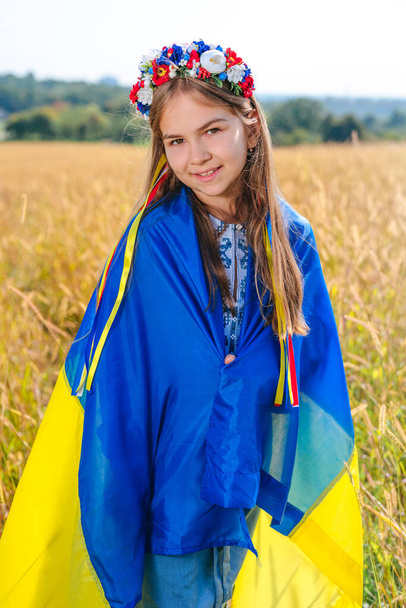 Little girl holding flag of Ukraine wearing wreath of flowers - Foto, imagen