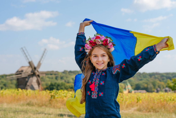 Girl wearing national clothes and wreath holding flag of Ukraine - Photo, Image