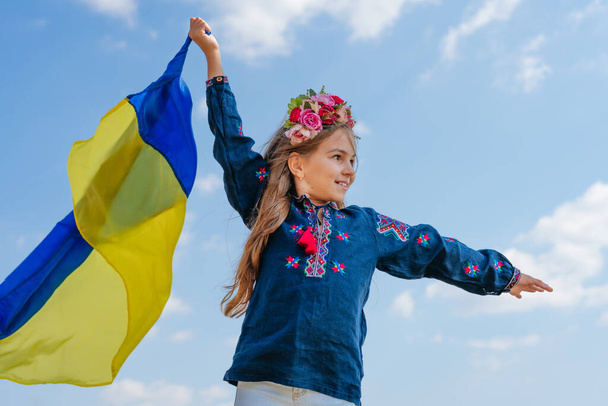 Girl wearing national clothes and wreath holding flag of Ukraine - 写真・画像