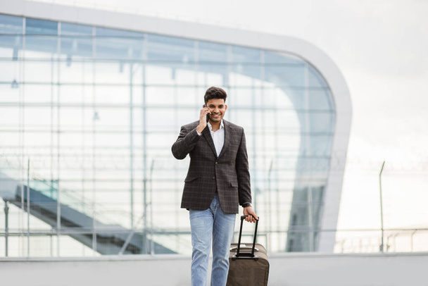 Indian business man walking outside to station or airport talking on the phone and carrying suitcase - Foto, Imagem