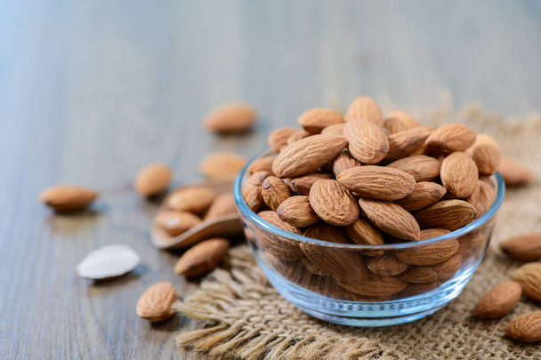Almonds nut with leaves in glass cup on wood background. They are highly nutritious and rich in healthy fats or High-density lipoprotein (HDL) cholesterol, antioxidants - Photo, Image