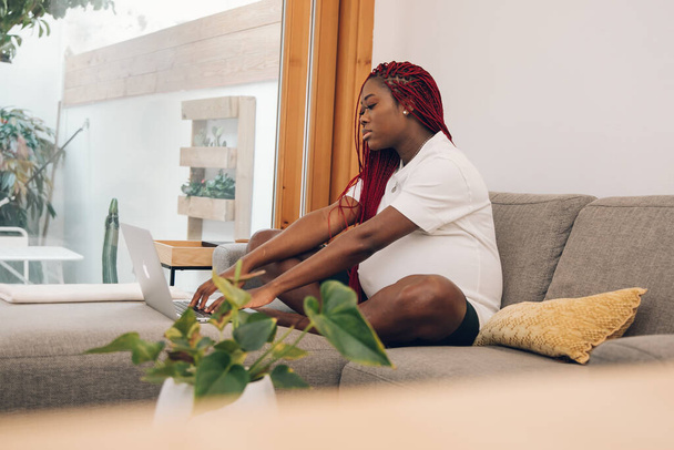 Schwarze schwangere Frau entspannt auf Sofa zu Hause mit seinem Laptop - Foto, Bild