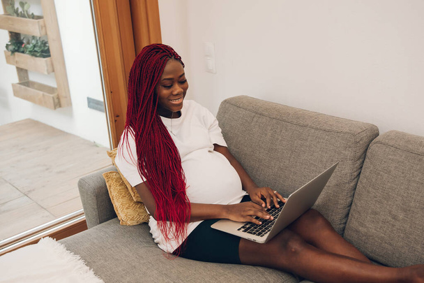 Černá těhotná žena relaxuje na pohovce doma se svým notebookem - Fotografie, Obrázek