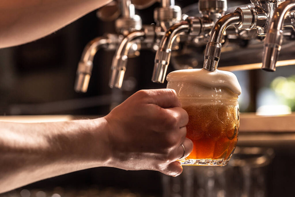 Woman holding mug of beer filled from the tap with foam floating out of the glass. - Foto, immagini