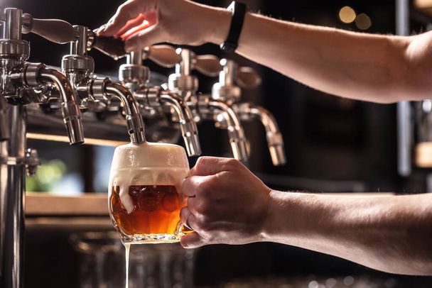 Hands of the pub employee tapping beer into a rounded mug. - Photo, image