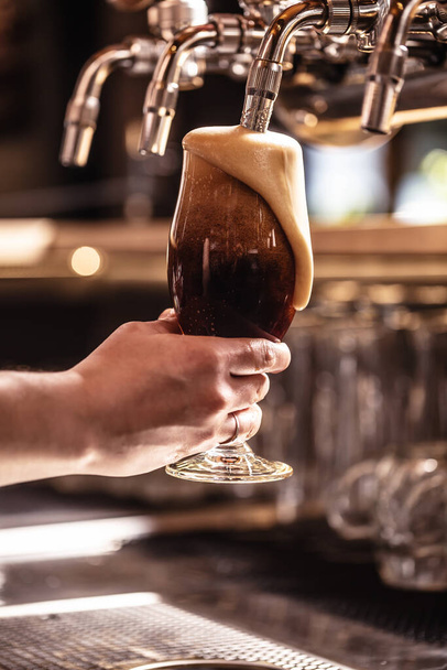 Foam pouring down the glass of a freshly tapped dark beer in a pub or a restaurant. - Zdjęcie, obraz