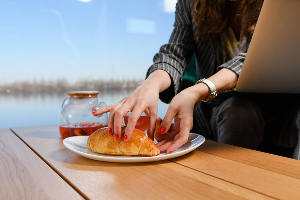 Woman hand hold breakfast croissant in plate on table, morning tea and bakery with beautiful water view in panoramic window - Fotoğraf, Görsel