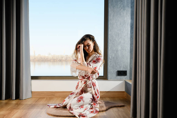 Tyttö japanilainen silkki puku istuu puulattia modernin kodin sisustus panoraama ikkuna, aamulla harjoitukset - Valokuva, kuva