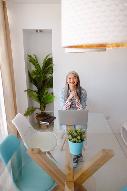 Joyeuse femme assise à la table avec ordinateur portable à la maison - Photo, image
