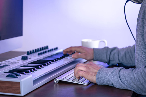 Αρσενικός μουσικός δημιουργεί μουσική χρησιμοποιώντας υπολογιστή και πληκτρολόγιο, χώρο εργασίας μουσικός. - Φωτογραφία, εικόνα