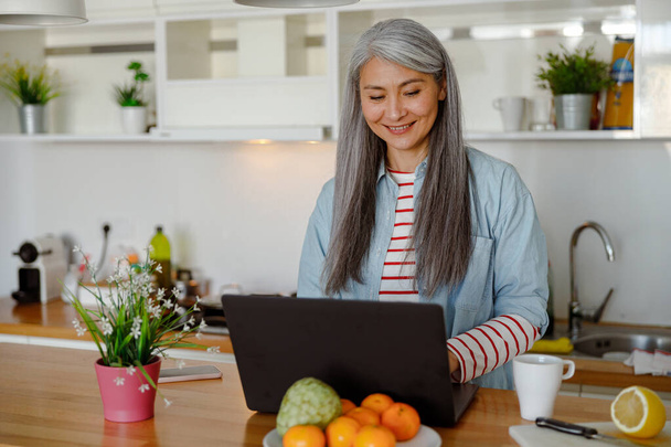 Cheerful woman using portable laptop in kitchen - Foto, immagini