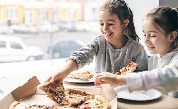 Happy little girls eat pizza in a cafe. - Φωτογραφία, εικόνα