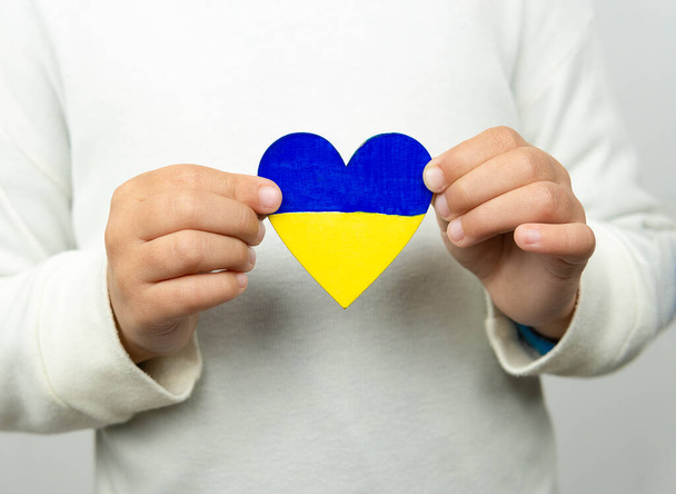 Chica sosteniendo un corazón con la bandera de Ucrania con ambas manos.Paz, Parar la guerra. - Foto, imagen