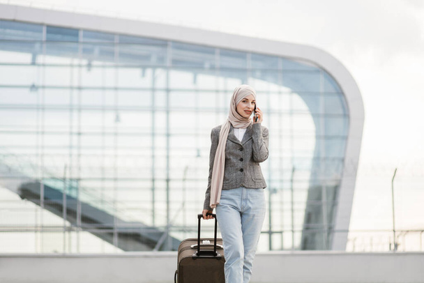 Pretty traveler tourist arabian woman in hijab carrying suitcase and talking phone - Foto, Imagem