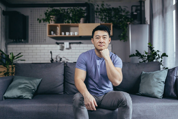 Portrait of a serious man at home, Asian man sitting on the couch looking intently at the camera - Foto, afbeelding