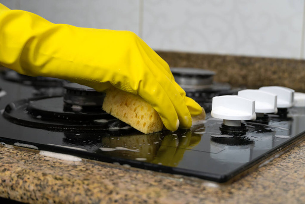 Крупним планом жіночу руку в жовтих рукавичках, що миють кухонну плиту за допомогою миючого засобу і губки
 - Фото, зображення