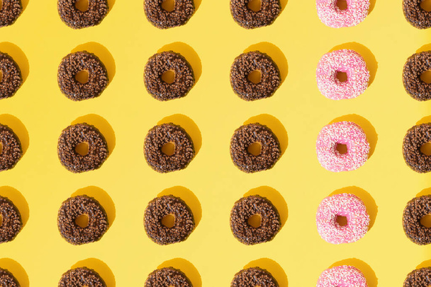 Arranged ring donuts with pink and chocolate glaze. Small white and brown crumbs on a yellow pastel background. Pattern. Flat lay. - Foto, Bild