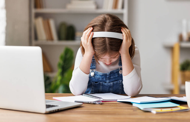 Zor bir görev üzerine düşünen ve masada ödev yaparken kafasına dokunan hayal kırıklığına uğramış bir kız. - Fotoğraf, Görsel