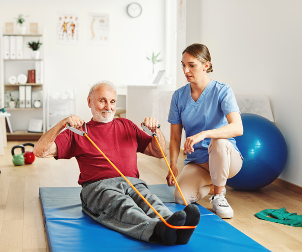 nurse doctor senior care exercise physical therapy exercising help assistence retirement home physiotherapy strech band clinic therapist elderly man - Valokuva, kuva