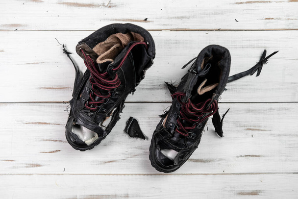 Torn worn shoes boots. Light wooden background. Torn, broken shoes. - Foto, Bild
