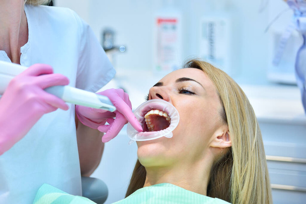 Pembe eldivenli kadın dişçi hastanın dişlerini 3D tarayıcıyla temizliyor. Kontrol ve stomatoloji kavramı - Fotoğraf, Görsel
