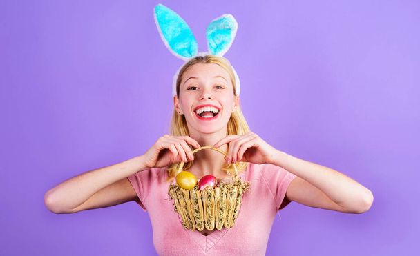 Великдень. Усміхнена дівчина в кролячих вухах з кошиком кольорових яєць. Жінка кролика. Весняні свята
. - Фото, зображення