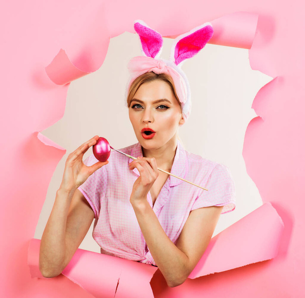 Pasqua. Donna sorpresa che dipinge uova. Ragazza sensuale in orecchie di coniglio con pennello e uovo rosa. - Foto, immagini