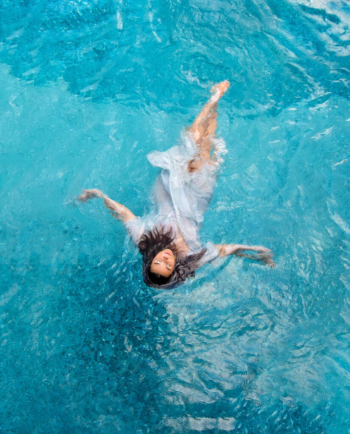 piękna młoda seksowna kobieta z chorobą witiligo pływanie w mokrej białej sukience w turkusowej wodzie basenu spa, przestrzeń do kopiowania - Zdjęcie, obraz
