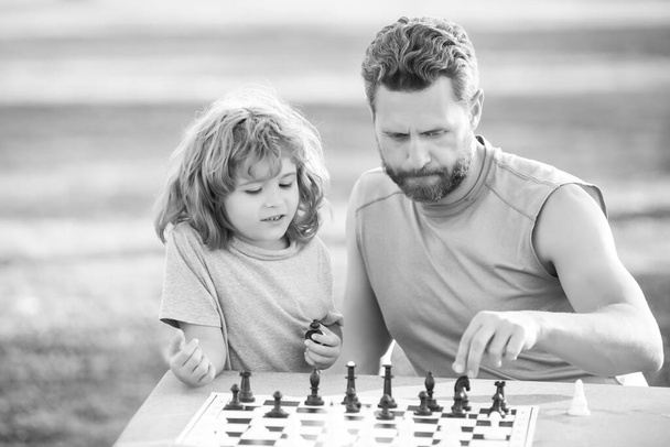 Son laying on grass and playing chess with father. Concentrated kid boy developing chess strategy, playing board game with parent. Games and activities for children. - Valokuva, kuva