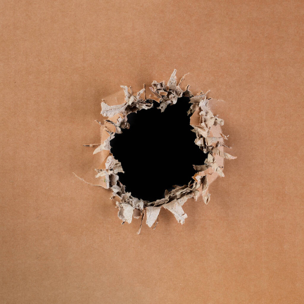 Prázdná lepenka s hrubou, roztrhanou a vyrvanou dírou uprostřed s prázdným černým prostorem - Fotografie, Obrázek