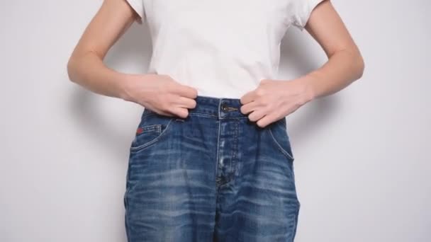 Donna felice che balla in jeans oversize su sfondo bianco. Il concetto di dieta, corretta alimentazione, perdita di peso e il corpo positivo. Slim donna mostrando sciolto jeans e la sua perdita di peso - Filmati, video