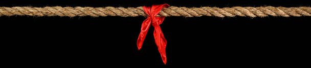 Long tug of war rope pulled tight, with red ribbon tie. Concept of conflict, competition, or rivalry.  Isolated on black. - Photo, Image