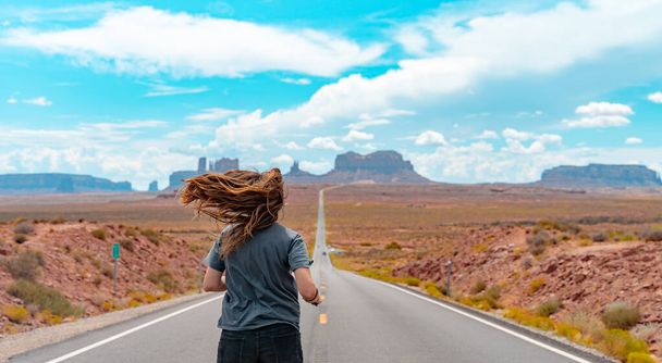 Attractive young woman from back view running in the middle of American straight road in the desert. - Foto, imagen
