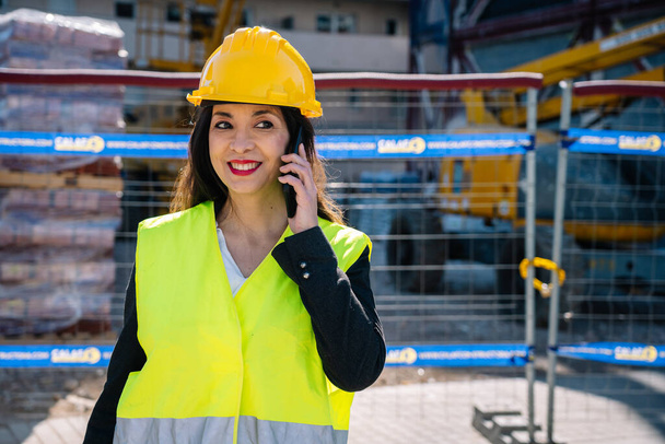 Feliz inspetor hispânico feminino tendo conversa telefônica no local de construção - Foto, Imagem