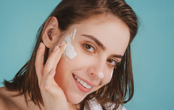 Beautiful young woman with clean fresh skin applying moisturizer cream on her pretty face. - Foto, afbeelding