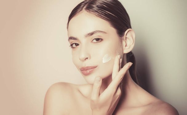 Beautiful woman spreading cream on her face. Skin cream concept. Facial care for female. Keep skin hydrated regularly moisturizing cream. Fresh healthy skin concept. Taking good care of her skin - Foto, Imagem