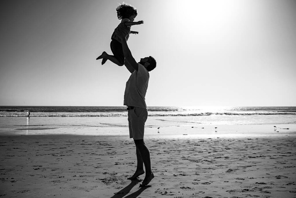 Father throws son up against the blue sky. Dad throwing child, silhouette on sunset. Concept of friendly family and of summer vacation. - Foto, Imagen