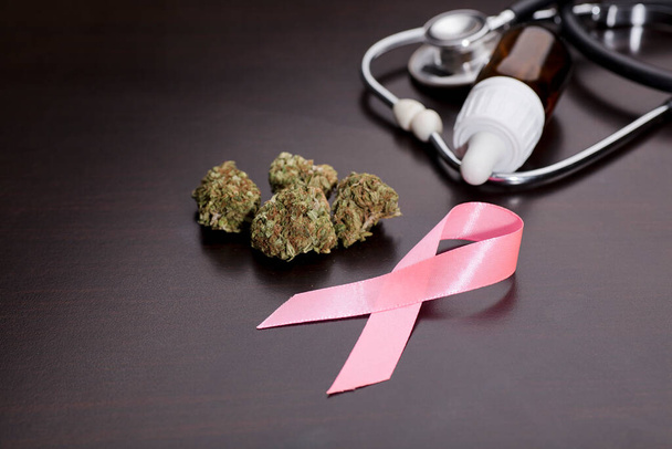 rakovina růžová stuha, lékařské marihuanové pupeny se stetoskopem, olejová láhev, hnědé pozadí. - Fotografie, Obrázek