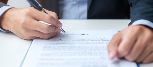 Businessman signing on contract documents after reading, man holding pen and approve on business report. Contract agreement, partnership and deal concepts - Photo, image