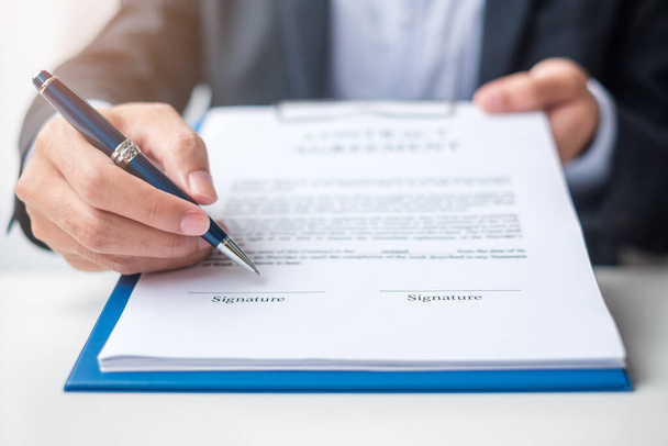 Бизнесмен подписывает контрактные документы после прочтения, человек держит ручку и утверждает по деловому отчету. Контрактное соглашение, партнерство и концепция сделок - Фото, изображение
