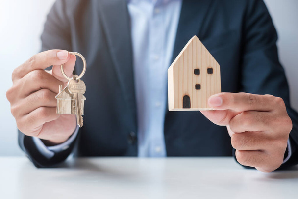 Geschäftsmann Hand hält Schlüssel mit hölzernem Home-Modell. Immobilien, Kauf und Verkauf, Objektversicherung, Miet- und Vertragskonzepte - Foto, Bild