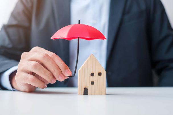 Empresario mano sosteniendo paraguas rojo cubierta de madera modelo Home. conceptos de bienes raíces, seguros y bienes raíces - Foto, Imagen
