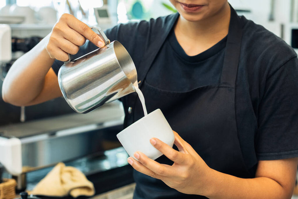 女性のバリスタはエプロンの制服を着てカフェカウンターでコーヒーを作ってる。女性マネージャーカフェスタートアップ中小企業. - 写真・画像