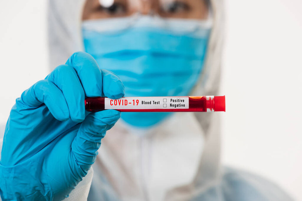 Ιατρικός επιστήμονας με στολή ΜΑΠ φορά μάσκα κρατώντας δοκιμαστικό σωλήνα Δείγμα αίματος από τον ιό του Coronavirus σε ένα νοσοκομειακό εργαστήριο για την ανάλυση απομονωμένο σε λευκό, φάρμακο COVID-19 έννοια πανδημία ξέσπασμα - Φωτογραφία, εικόνα